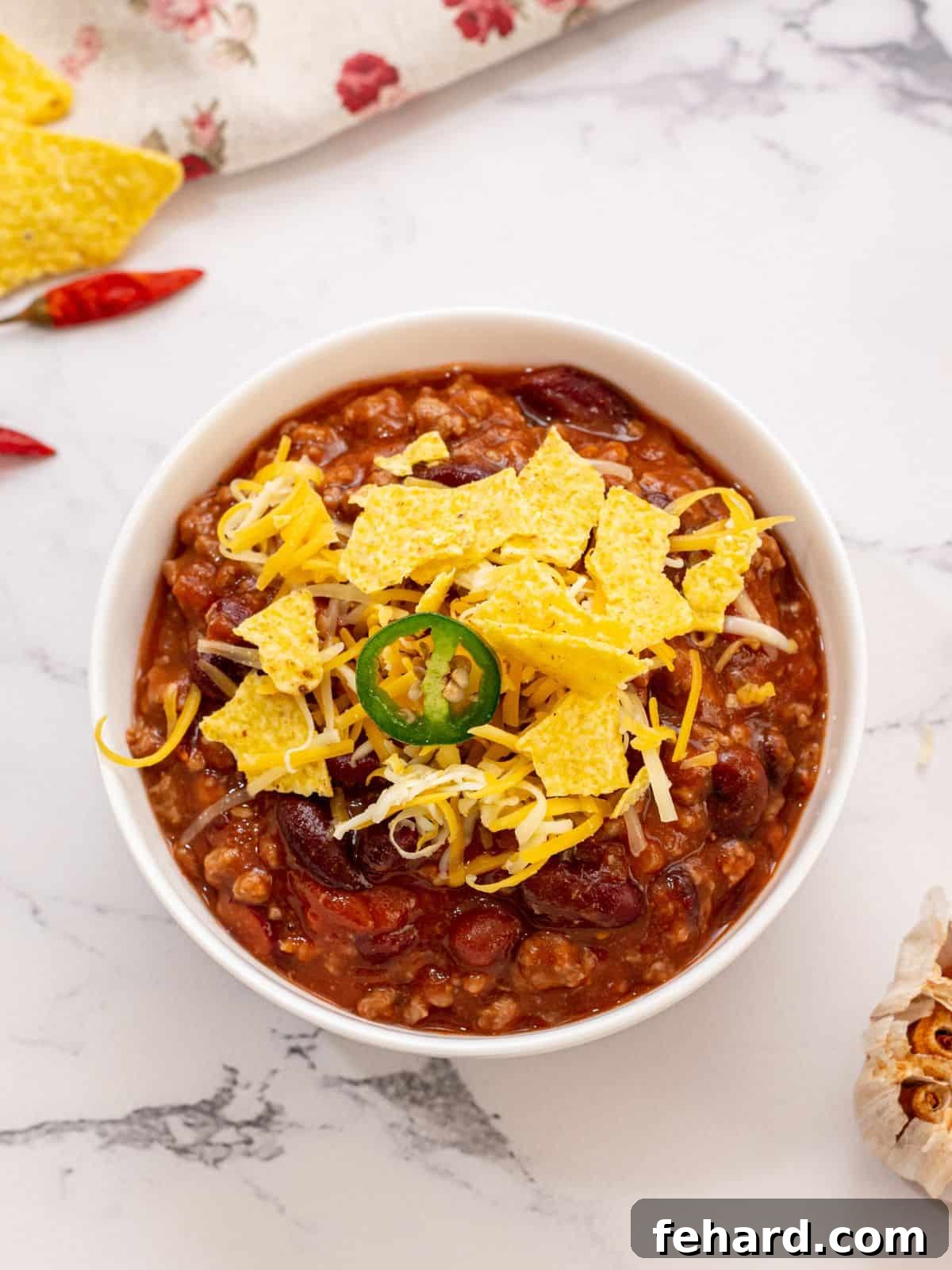 A vibrant bowl of homemade Crockpot Chili, generously topped with crispy corn chips, shredded cheddar cheese, and thinly sliced fresh jalapeño, ready to be enjoyed.