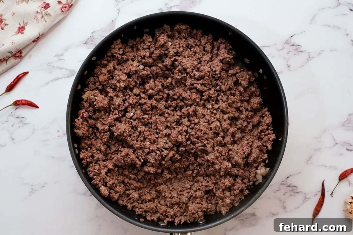 Ground beef, diced yellow onion, and minced garlic sautéing in a hot skillet, releasing rich aromas and developing caramelized flavors.