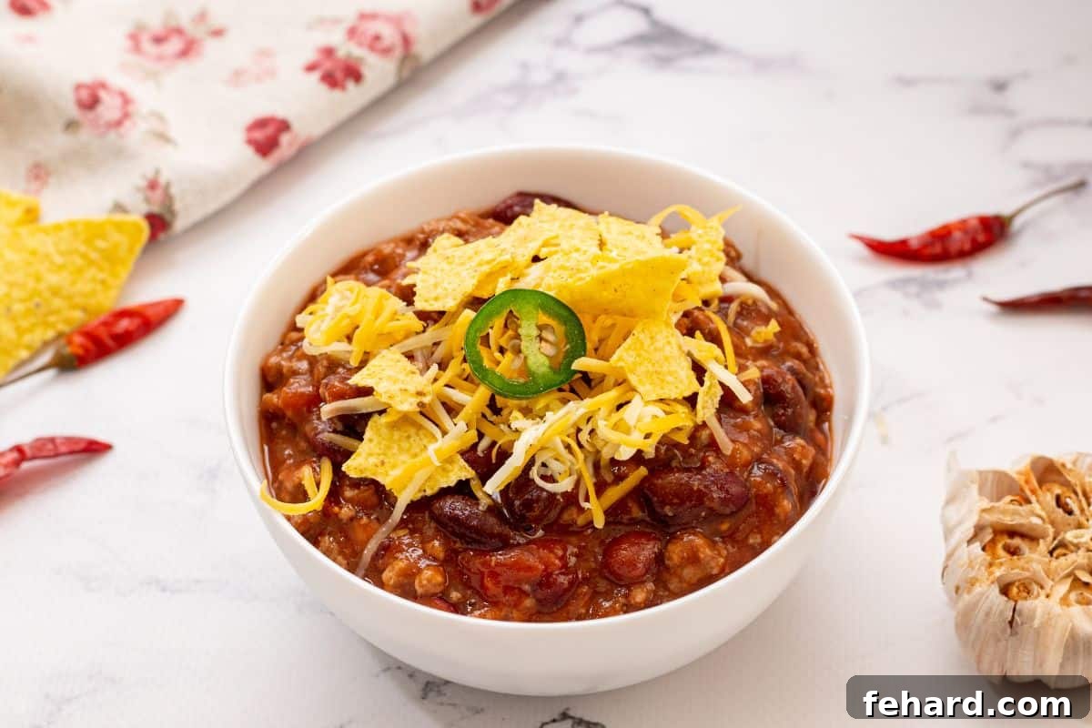 A delectable bowl of Crockpot Chili, artfully garnished with a colorful array of corn chips, a generous sprinkle of golden shredded cheese, and vibrant slices of fresh jalapeño, highlighting its irresistible appeal.