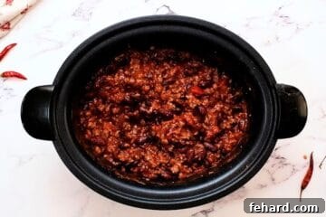 Ingredients for crockpot chili, including beef, beans, and rich tomato sauce, neatly combined in the base of a slow cooker.