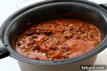 A crockpot gently simmering with a hearty beef and bean chili, signifying the long, slow cooking process for maximum flavor.