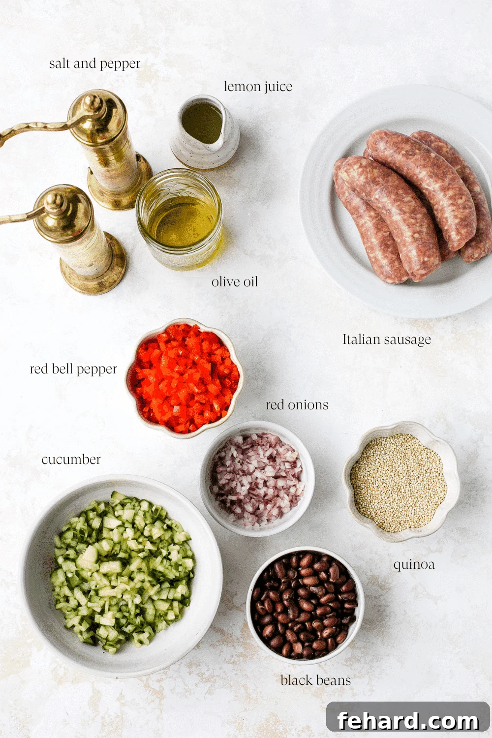 A top-down view of various ingredients for quinoa salad neatly arranged on a white surface, including cooked quinoa, chopped vegetables, black beans, and sausages.