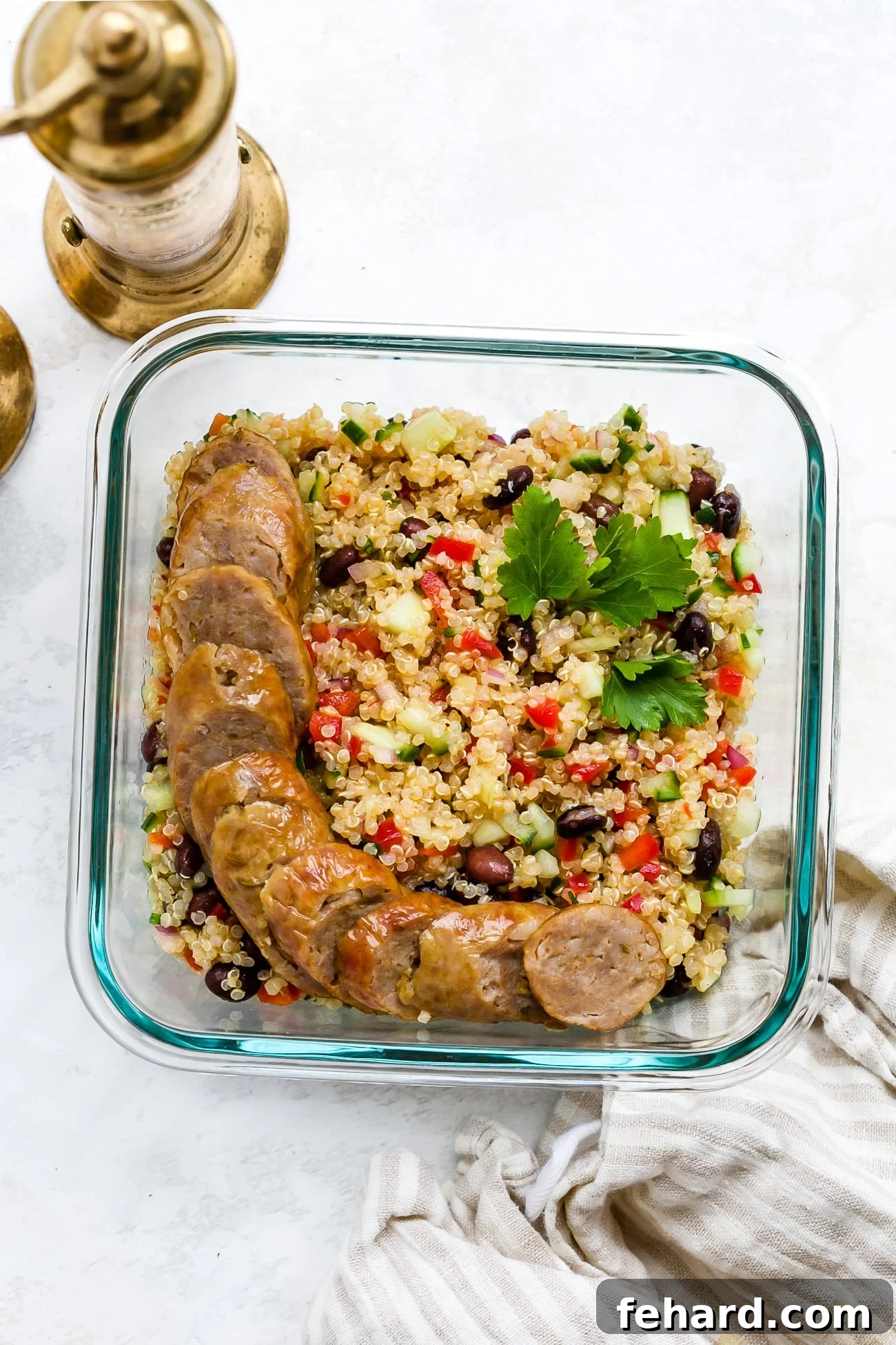 A portion of quinoa salad with sausage in a clear meal-prep container, ready for storage.