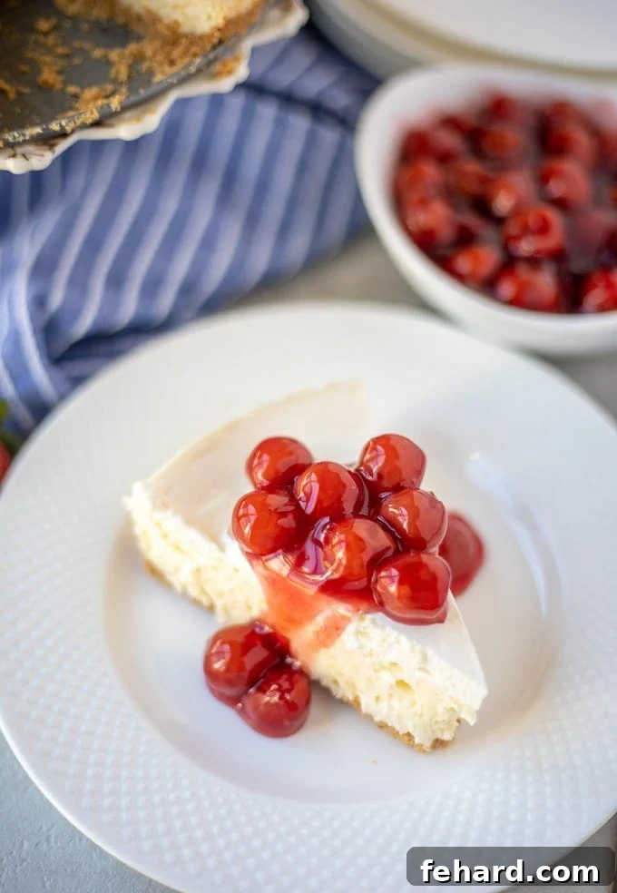 Best Classic Cheesecake Recipe A slice of classic cheesecake on a white plate with fresh cherries on top, emphasizing its creamy texture.