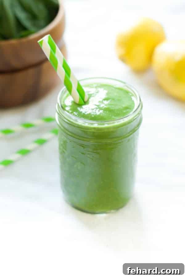 A glass jar containing pineapple green smoothie with two green paper straws, presented beautifully.