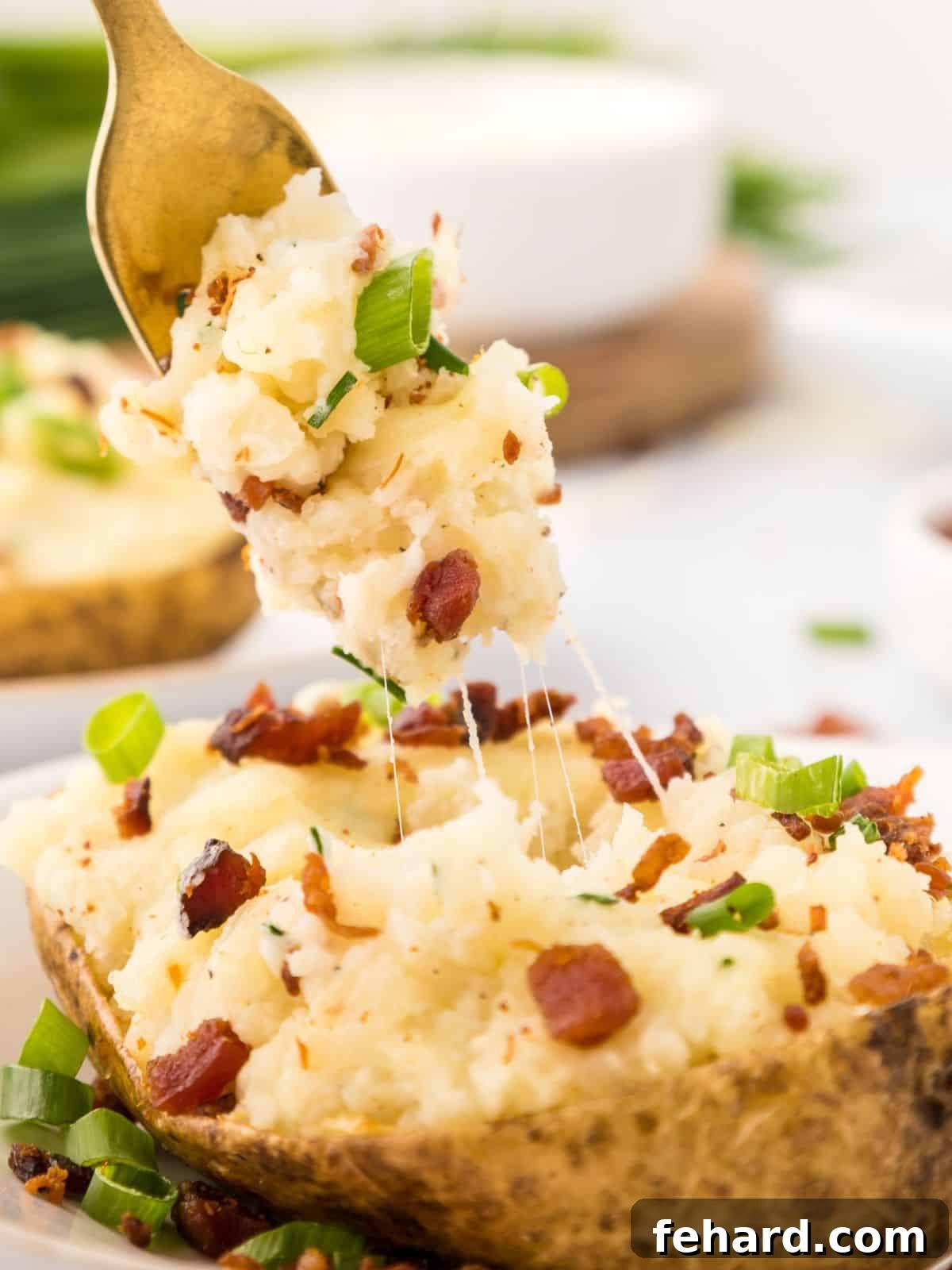 Fork of cheesy potato filling coming out of a Twice-Baked Potato topped with white cheddar, bacon, and green onions on a white plate.