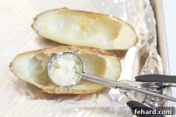 A small cookie scoop removing the fluffy flesh from a baked potato half on a baking sheet.