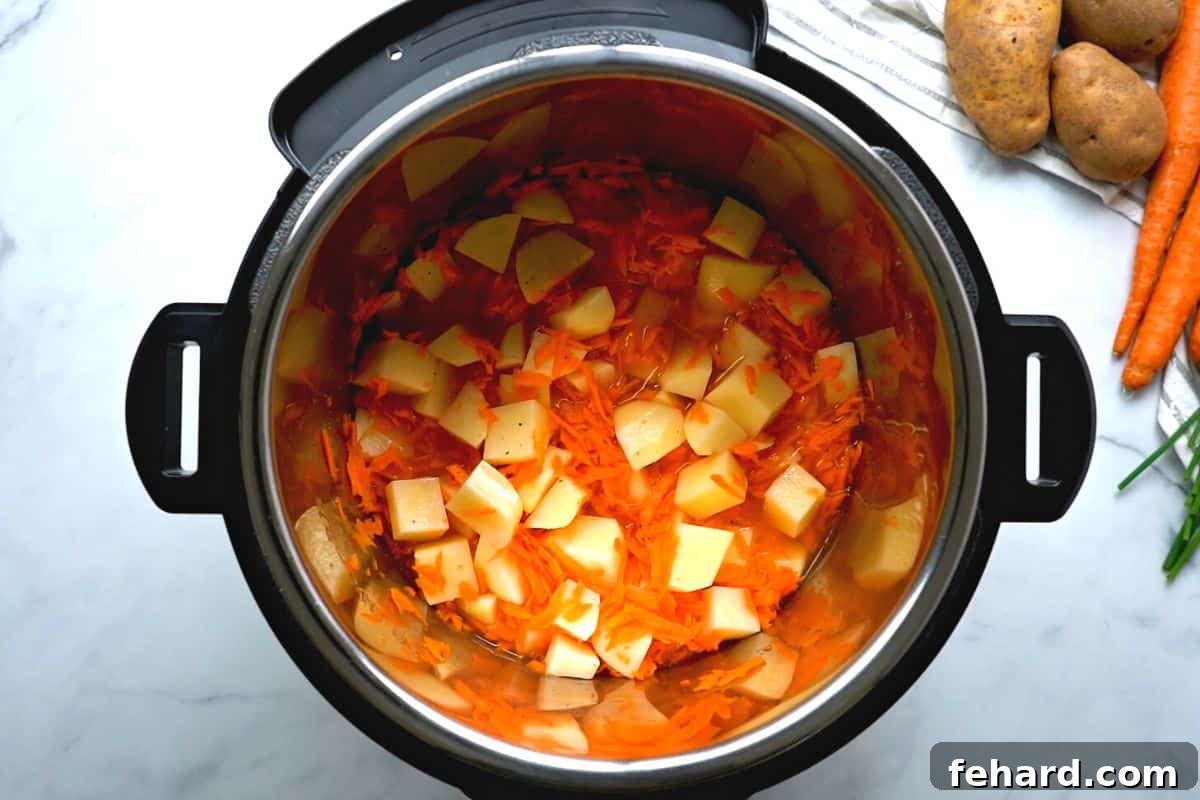Instant Pot Potato Soup Carrots, broth, potatoes, and seasonings inside inner pot.