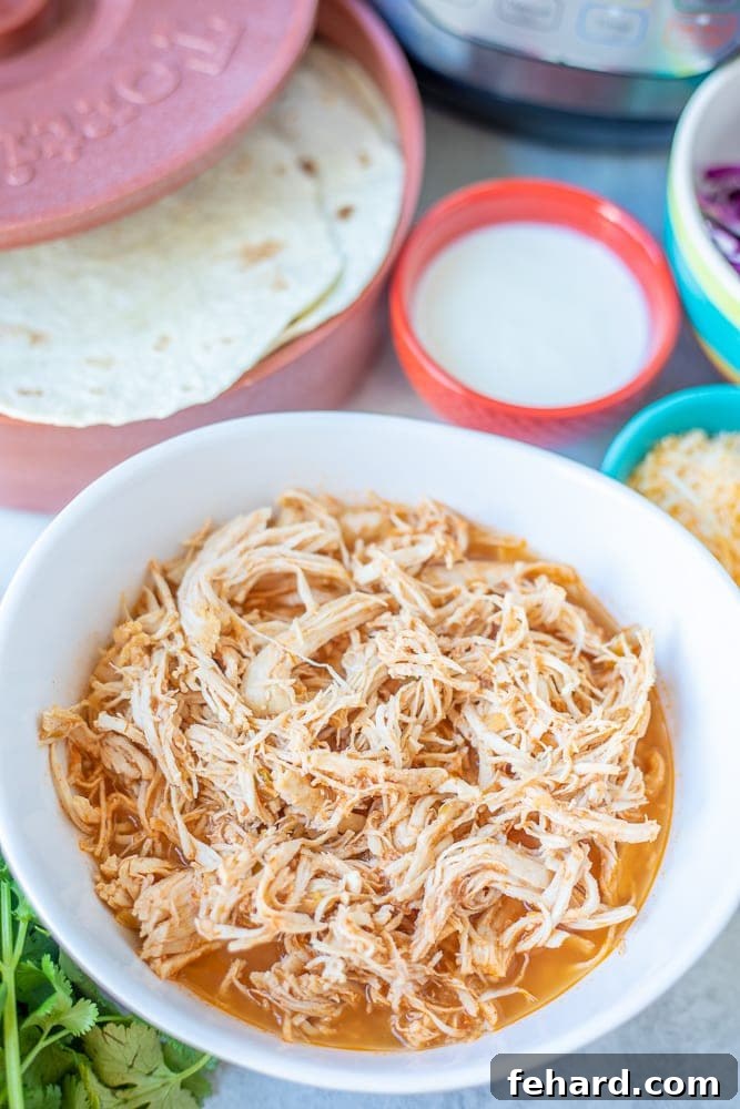 Bowl of Instant Pot Tex Mex Shredded Chicken, with an Instant Pot and various taco toppings in the background, ready to be served.