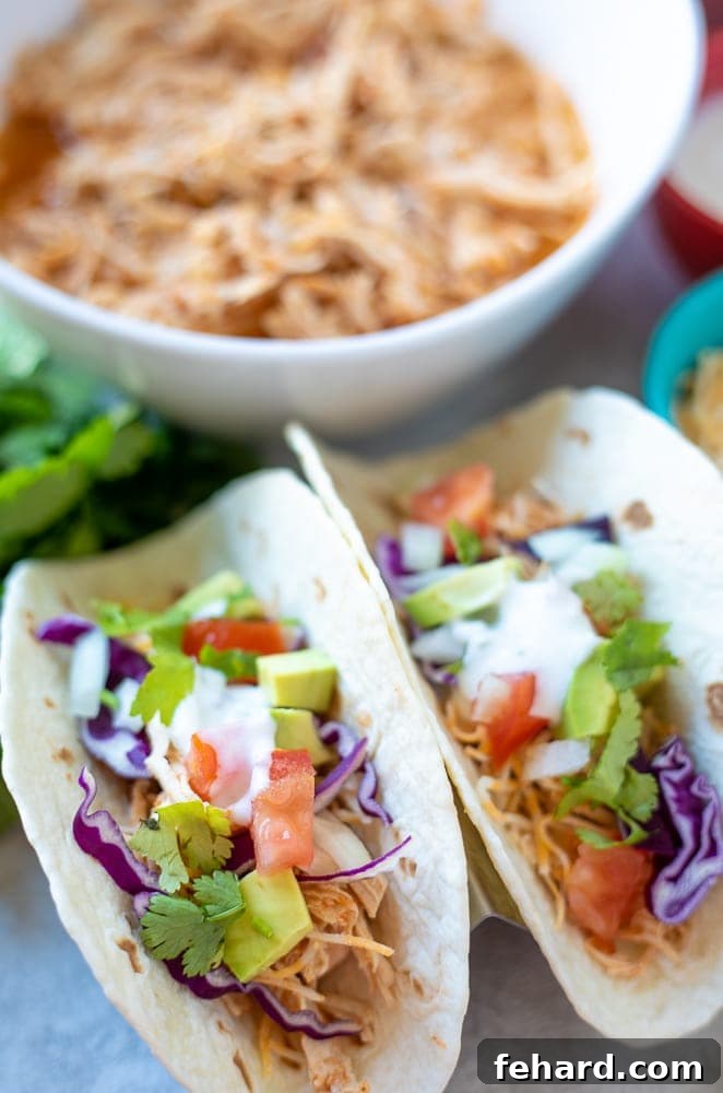 Instant Pot Shredded Taco meat served on warm flour tortillas, garnished with vibrant purple cabbage, diced avocado, and cherry tomatoes.
