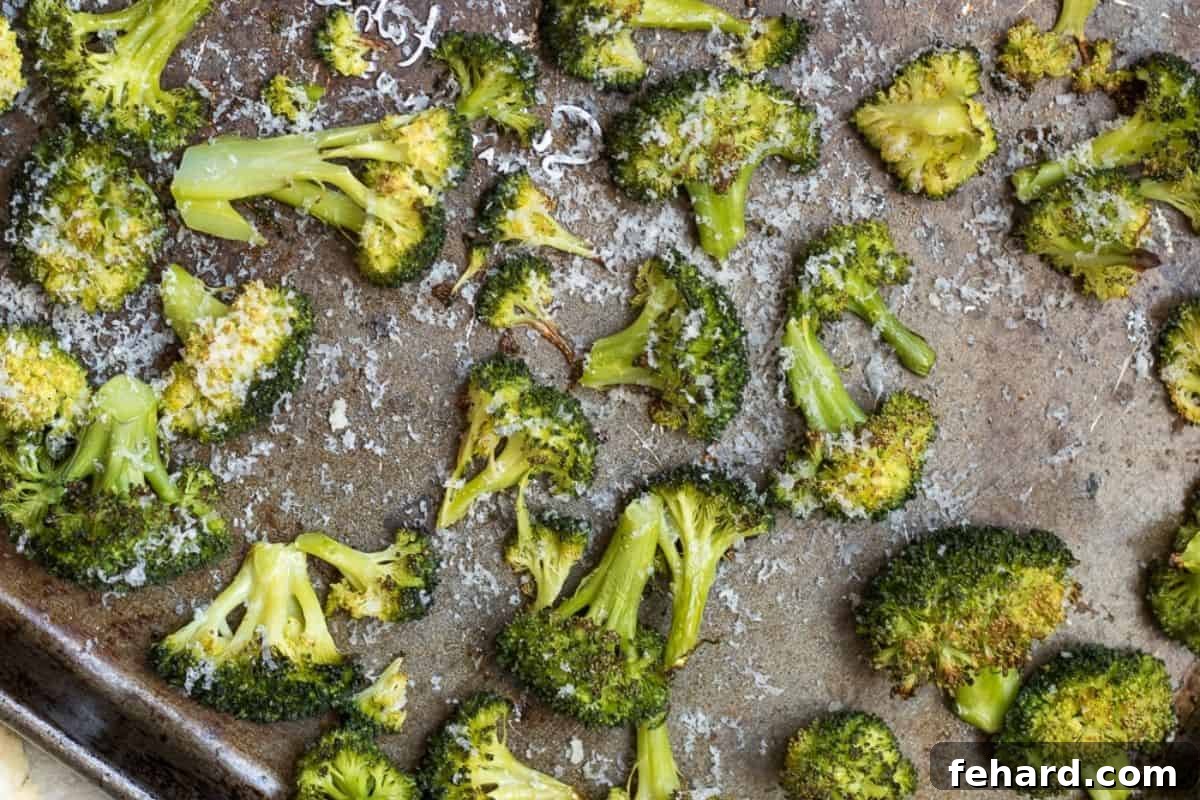 Roasted Broccoli on sheet pan with freshly grated Parmesan Cheese melting over it, and a lemon wedge.