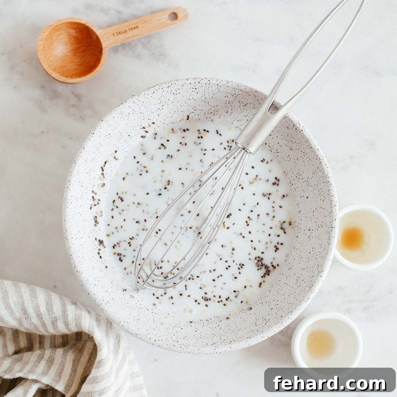 Dreamy Raspberry Chia Pudding 4 Photo showing chia seeds being mixed with coconut milk, vanilla extract, maple syrup, and salt in a bowl.