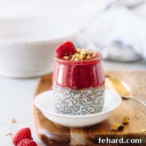 A jar of chia seed pudding with raspberry puree, fresh raspberries, and pistachios on top, ready to eat.