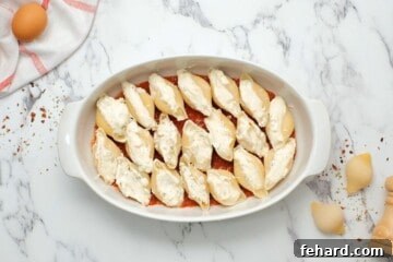Classic Italian Stuffed Shells 9 Stuffed cooked jumbo shells arranged neatly in a baking dish lined with spaghetti sauce, ready for the next layer.