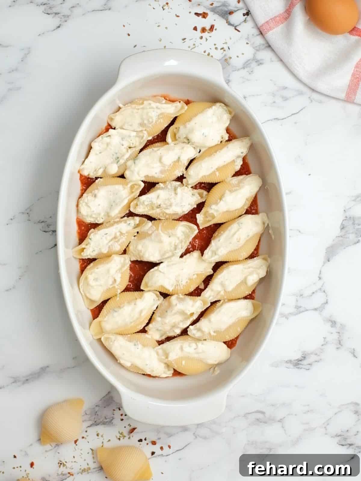 Classic Italian Stuffed Shells 3 Stuffed cooked jumbo shells arranged neatly in a baking dish lined with spaghetti sauce.