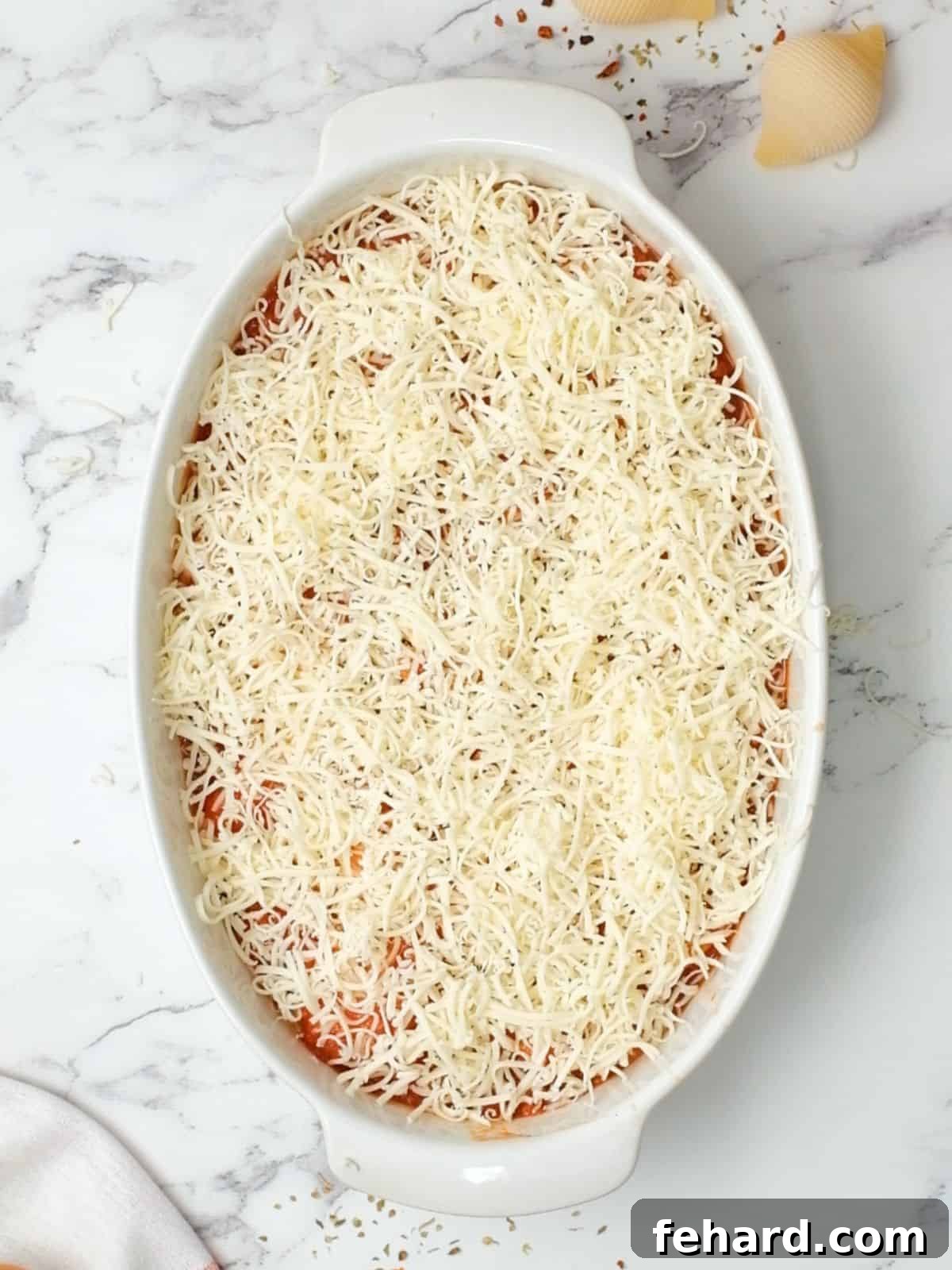 Classic Italian Stuffed Shells 4 Stuffed shells generously topped with marinara sauce and shredded mozzarella cheese in an oval baking dish, ready for the oven.