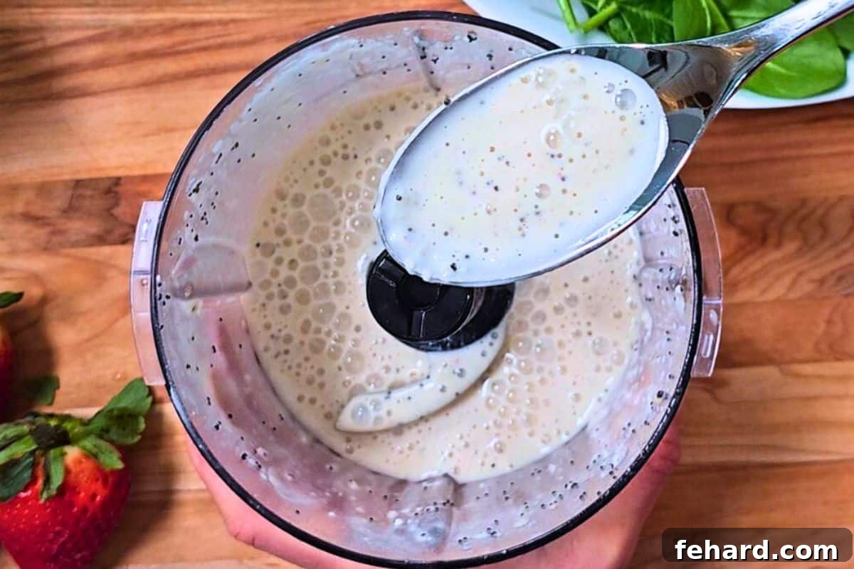 Blending Poppy Seed Dressing with Greek Yogurt Creamy poppy seed dressing in a small food processor with a spoon showing the smooth dressing.
