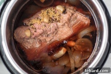 Cooked Corned Beef inside inner pot with onions and garlic.