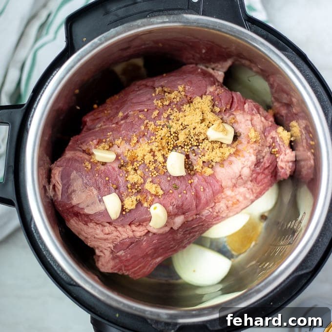 Corned beef brisket layered on onions, topped with pickling spices, garlic, and brown sugar inside the Instant Pot inner pot, ready for liquid.