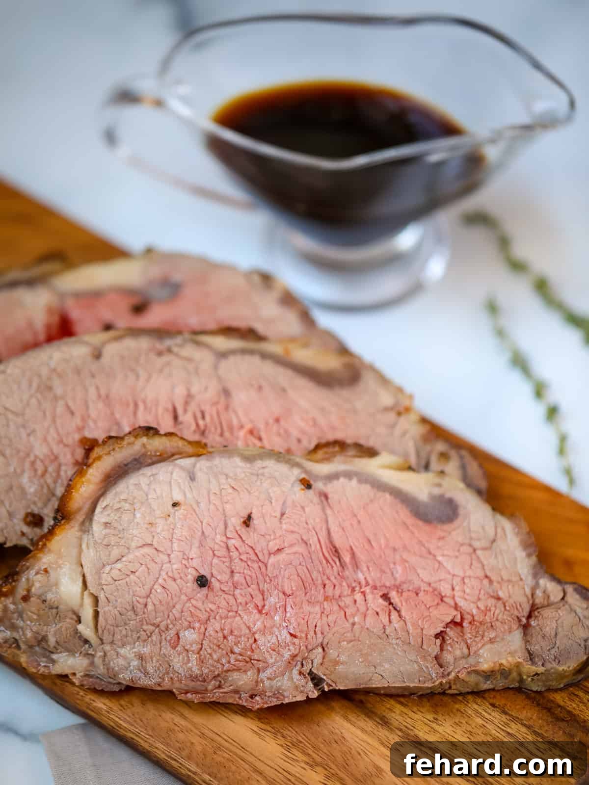 Perfectly sliced New York Strip Roast on a cutting board, with a small bowl of savory au jus in the background.