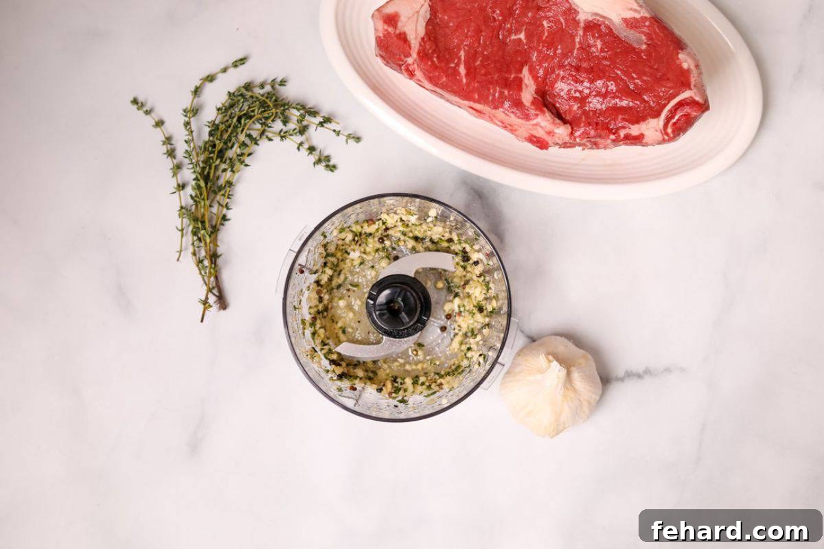 A mini food processor containing fresh thyme, peeled garlic, and olive oil, blended into a rich seasoning paste for steak.