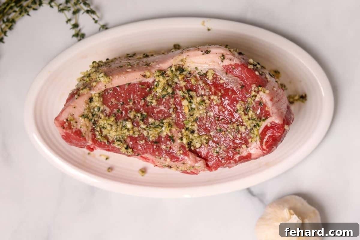 A large New York Strip Roast, generously seasoned with the garlic-herb rub, resting on a white platter.