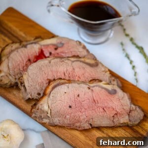 Sliced New York Strip Roast on a cutting board with au jus in the background.