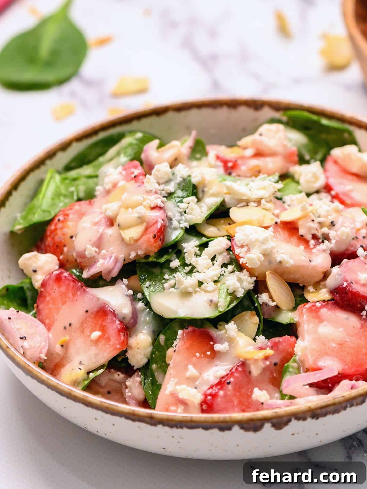 Spinach salad in serving dish topped with strawberies and poppyseed dressing.
