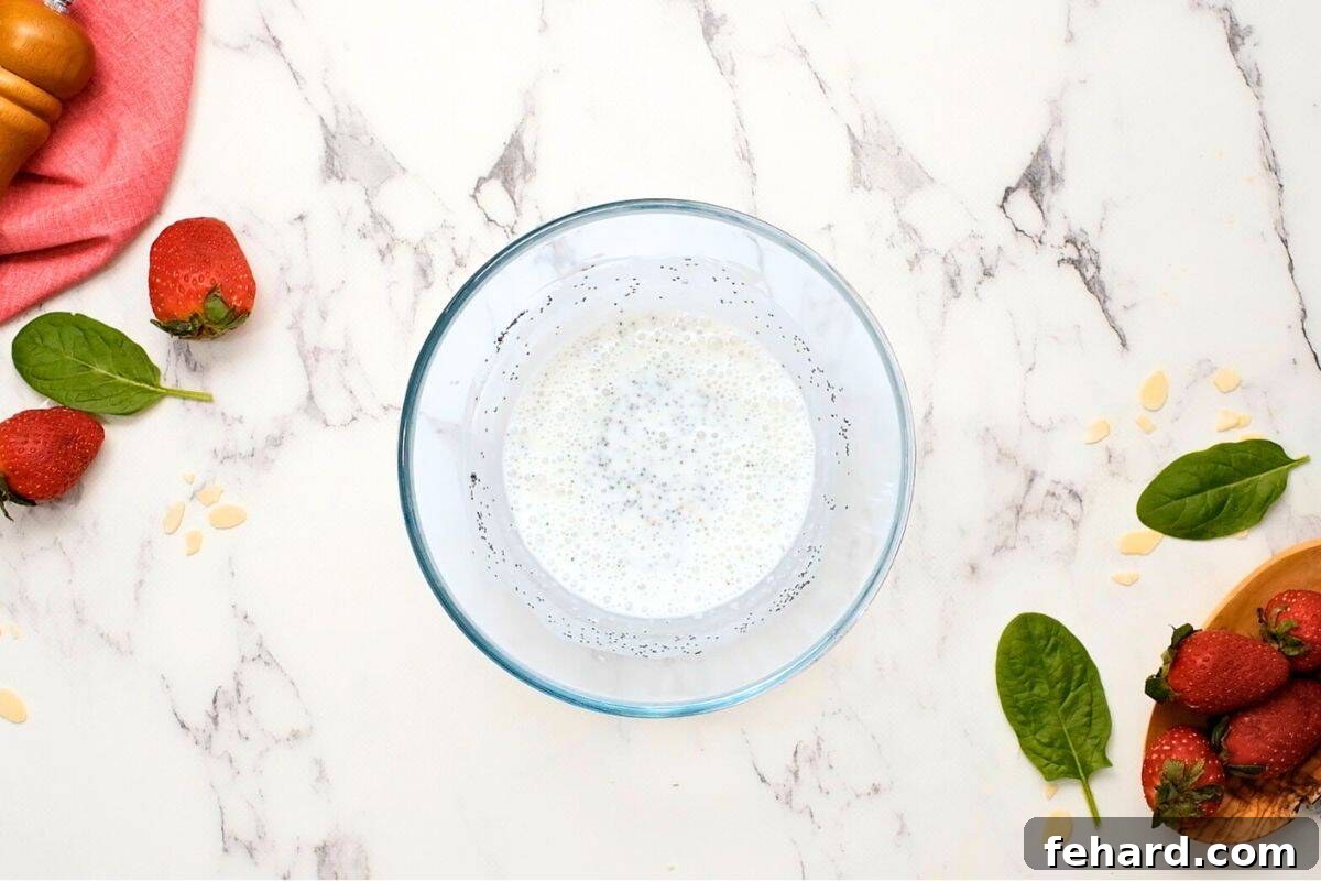 Homemade creamy poppy seed dressing in mixing bowl next to fresh strawberries. 