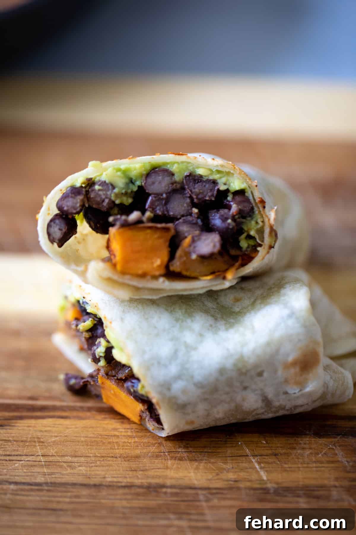 A deliciously filled sweet potato and black bean burrito, garnished with fresh avocado slices.