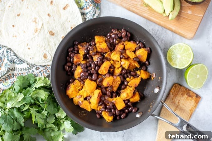 Skillet filled with seasoned black bean and sweet potato mixture, next to a stack of warm tortillas ready for assembly.