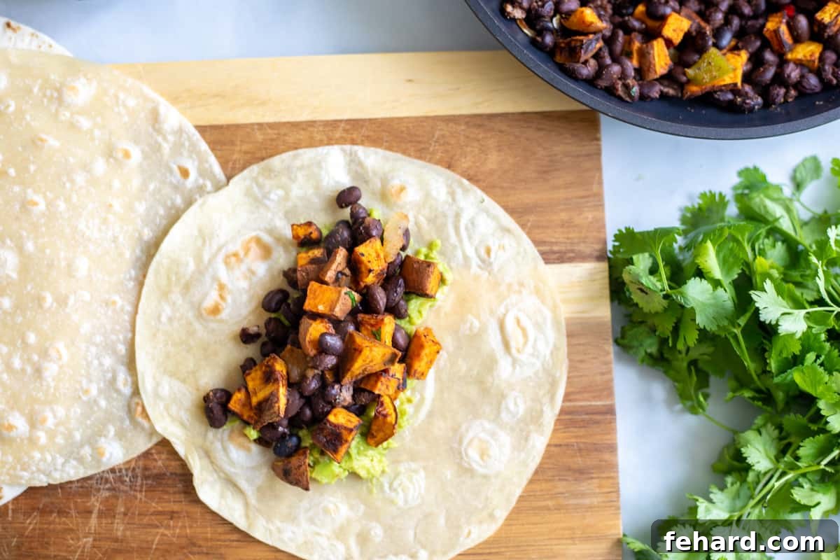 A warm flour tortilla topped generously with a savory sweet potato and black bean filling, ready to be wrapped into a delicious burrito.
