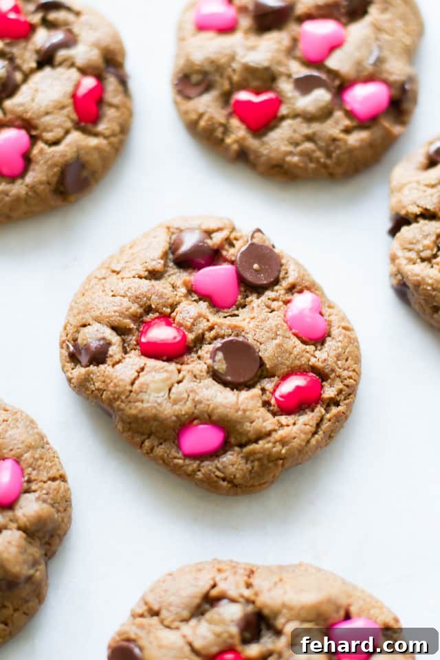 Overhead close-up of a single Valentine's Day gluten-free chocolate chip cookie with sunflower butter and heart candies, surrounded by other cookies.