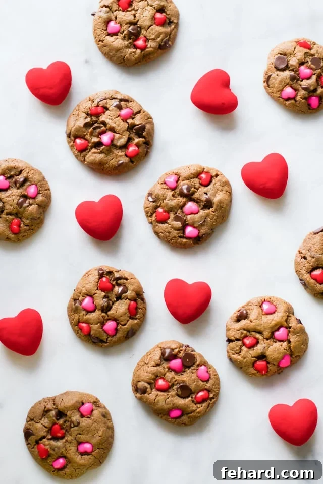 Overhead view of ten freshly baked Valentine's Day gluten-free chocolate chip cookies with heart candies arranged around them.