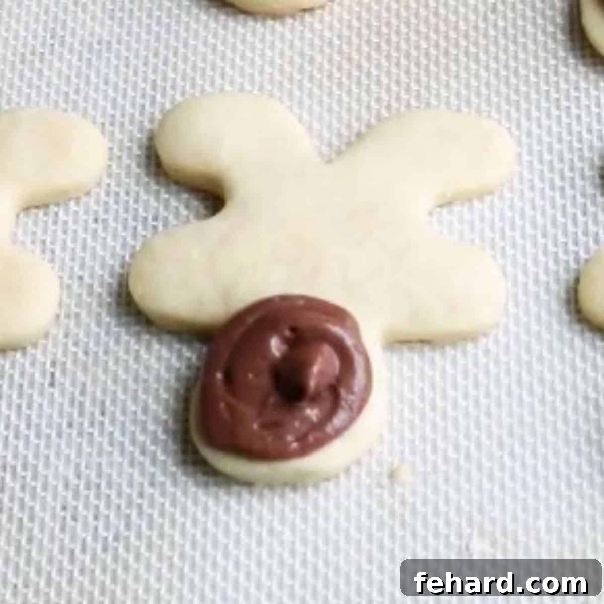 An upside-down gingerbread man cookie with a piped circle of chocolate frosting on its head, marking the reindeer's face area.