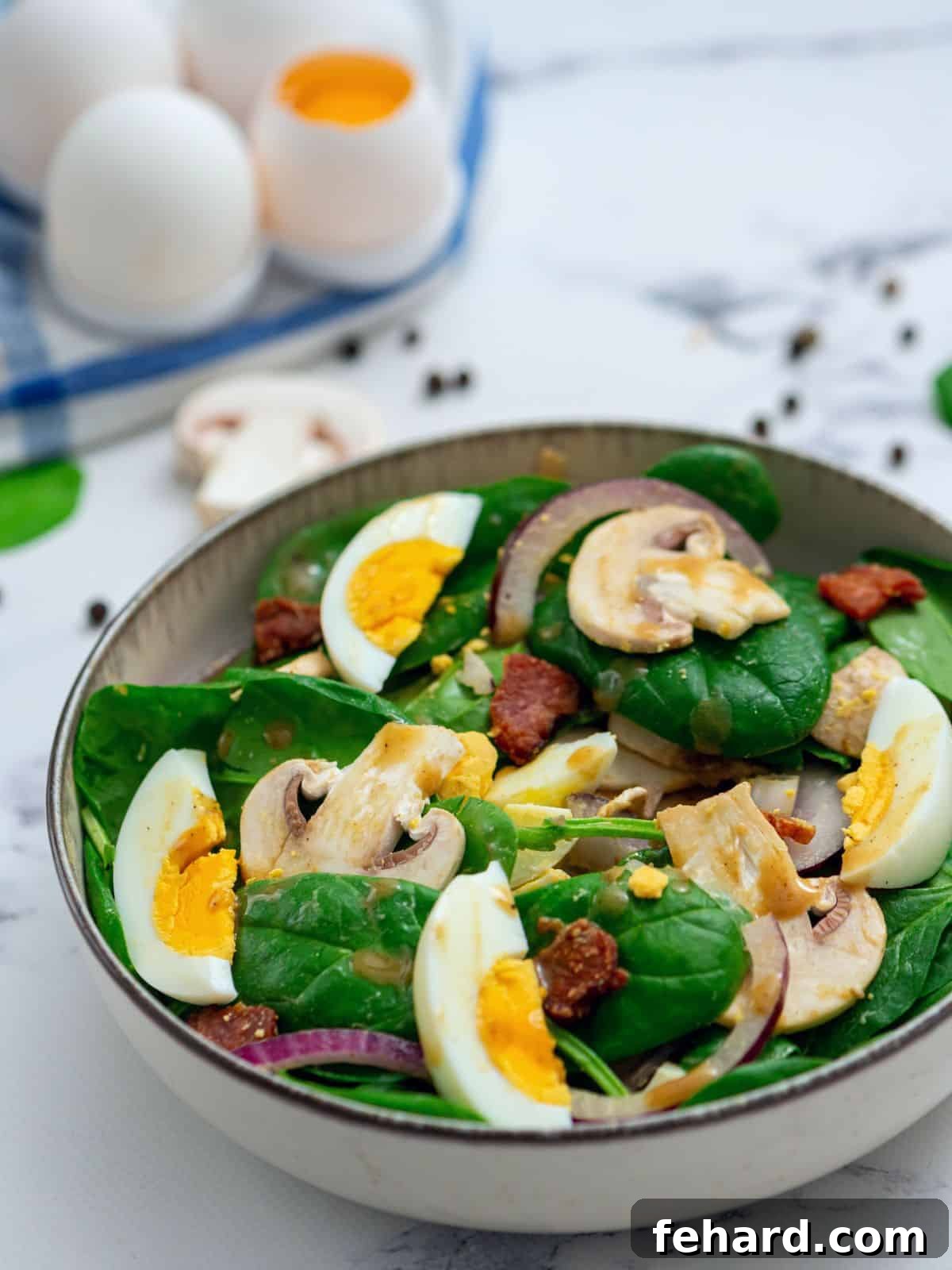 Spinach Bacon Salad - Perfect for Any Occasion A beautiful bowl of vibrant spinach salad generously topped with warm bacon dressing, perfectly sliced hard-boiled eggs, and crisp bacon crumbles.