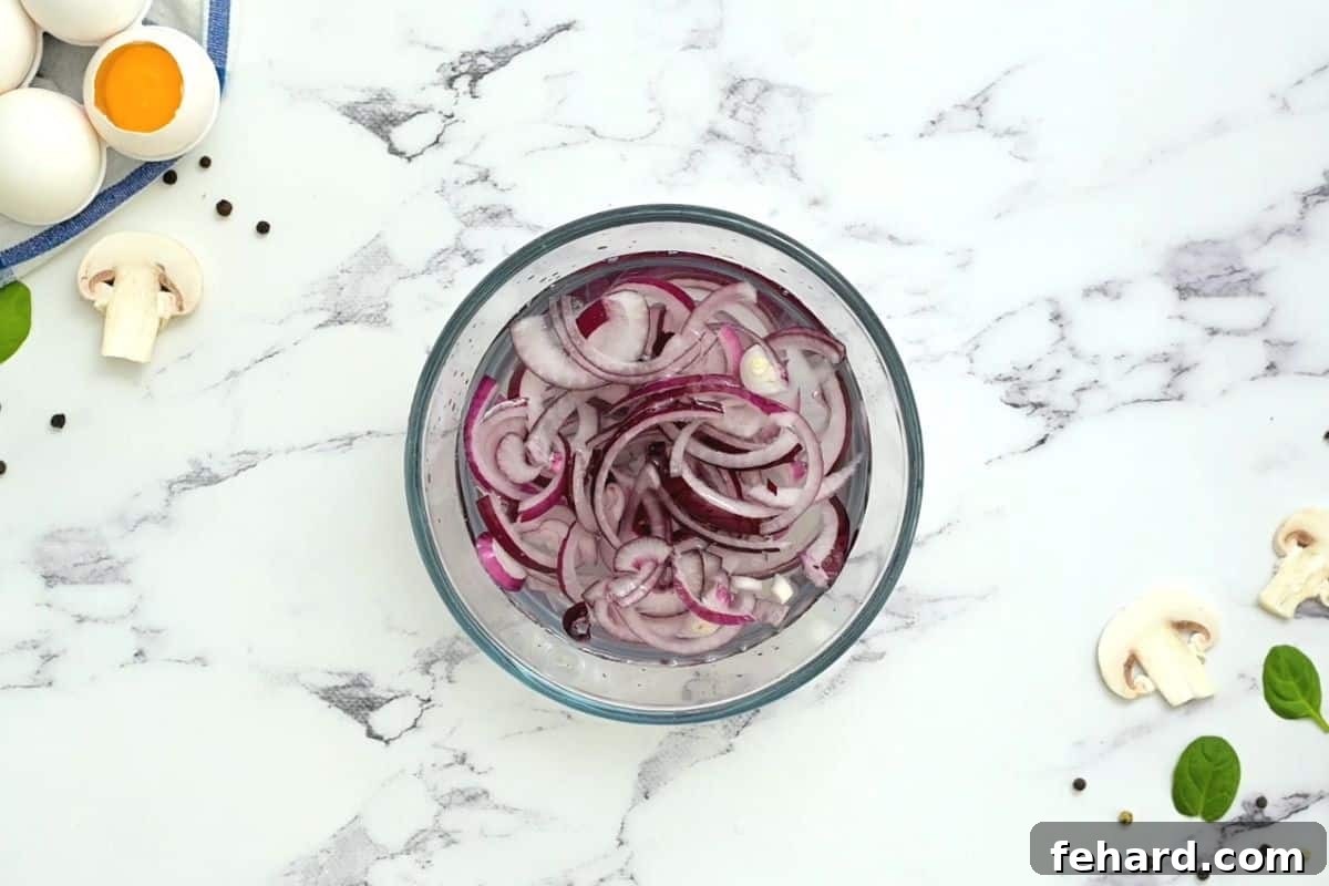 Preparing Red Onions for Salad Thinly sliced red onions soaking in cold water in a small glass bowl.