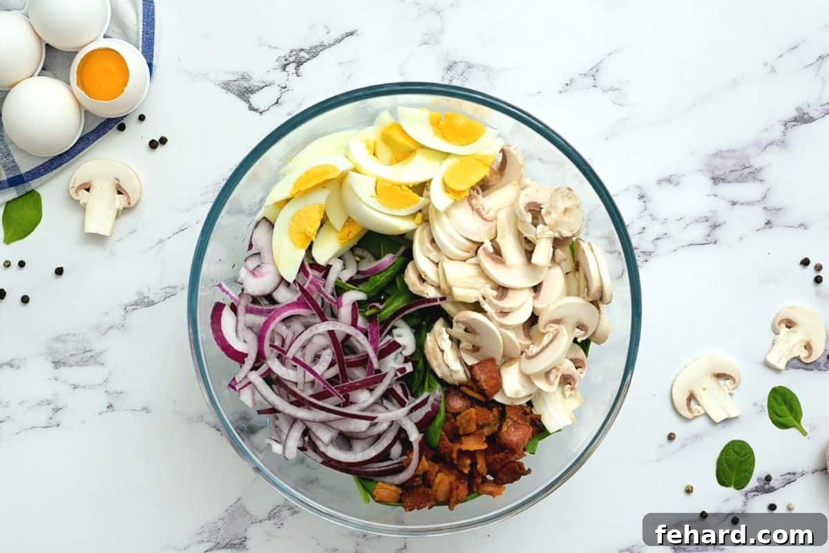 Assembling the Best Bacon Spinach Salad A large clear serving bowl filled with spinach, red onions, sliced hard-boiled eggs, mushrooms, and crispy bacon, ready for dressing.