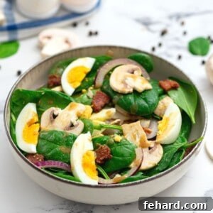 Spinach salad topped with bacon, mushrooms, red onions, and hard-boiled eggs.