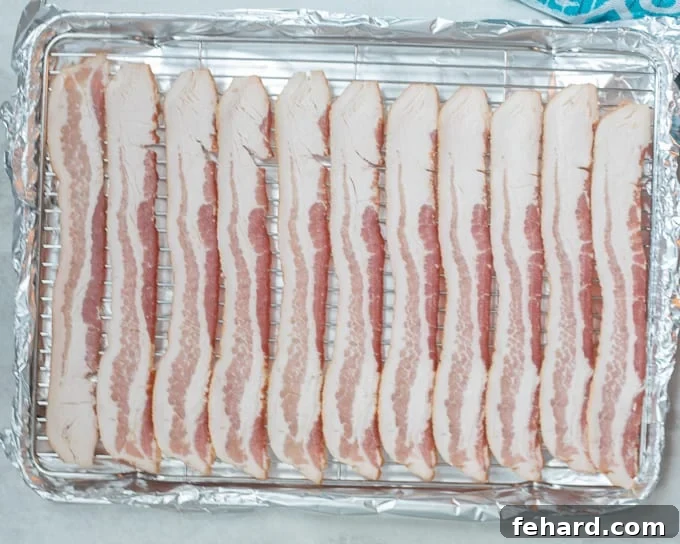 Raw bacon strips neatly arranged in a single layer on a baking sheet with a rack.