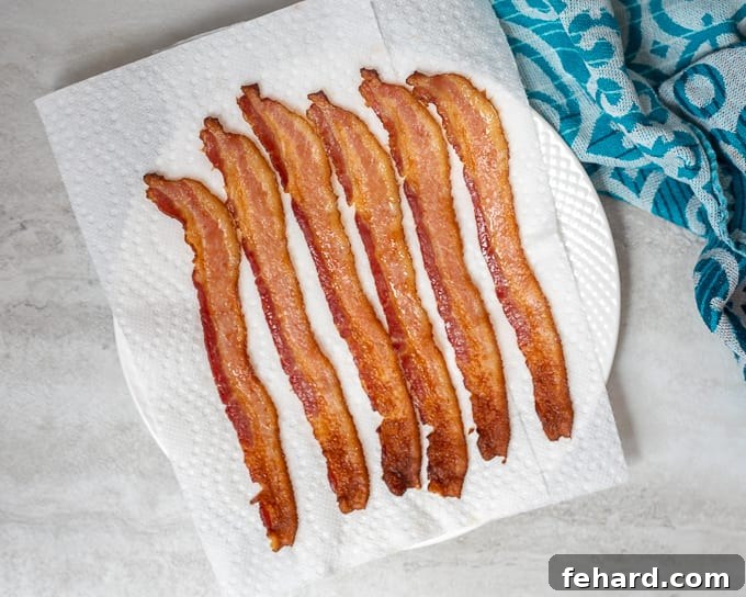 Freshly baked bacon resting on a plate lined with paper towels to drain excess fat.