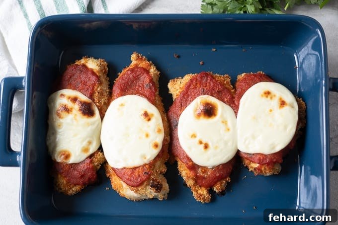 Baked Chicken Parmesan topped with marinara and melted mozzarella in a casserole dish.