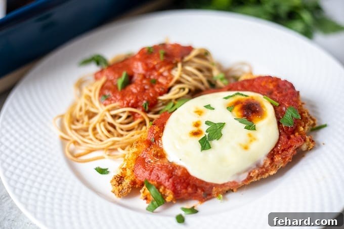 Baked Chicken Parmesan served on a white plate next to a generous serving of spaghetti.