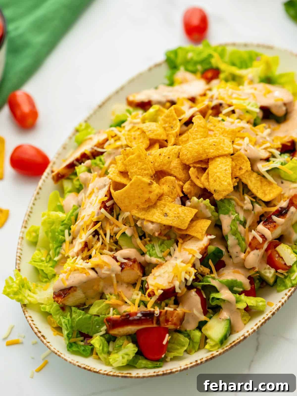 A vibrant BBQ Chicken Salad presented on a serving platter, featuring grilled chicken strips, crisp lettuce, corn, tomatoes, shredded cheese, and crunchy tortilla chips, all drizzled with BBQ Ranch Dressing.