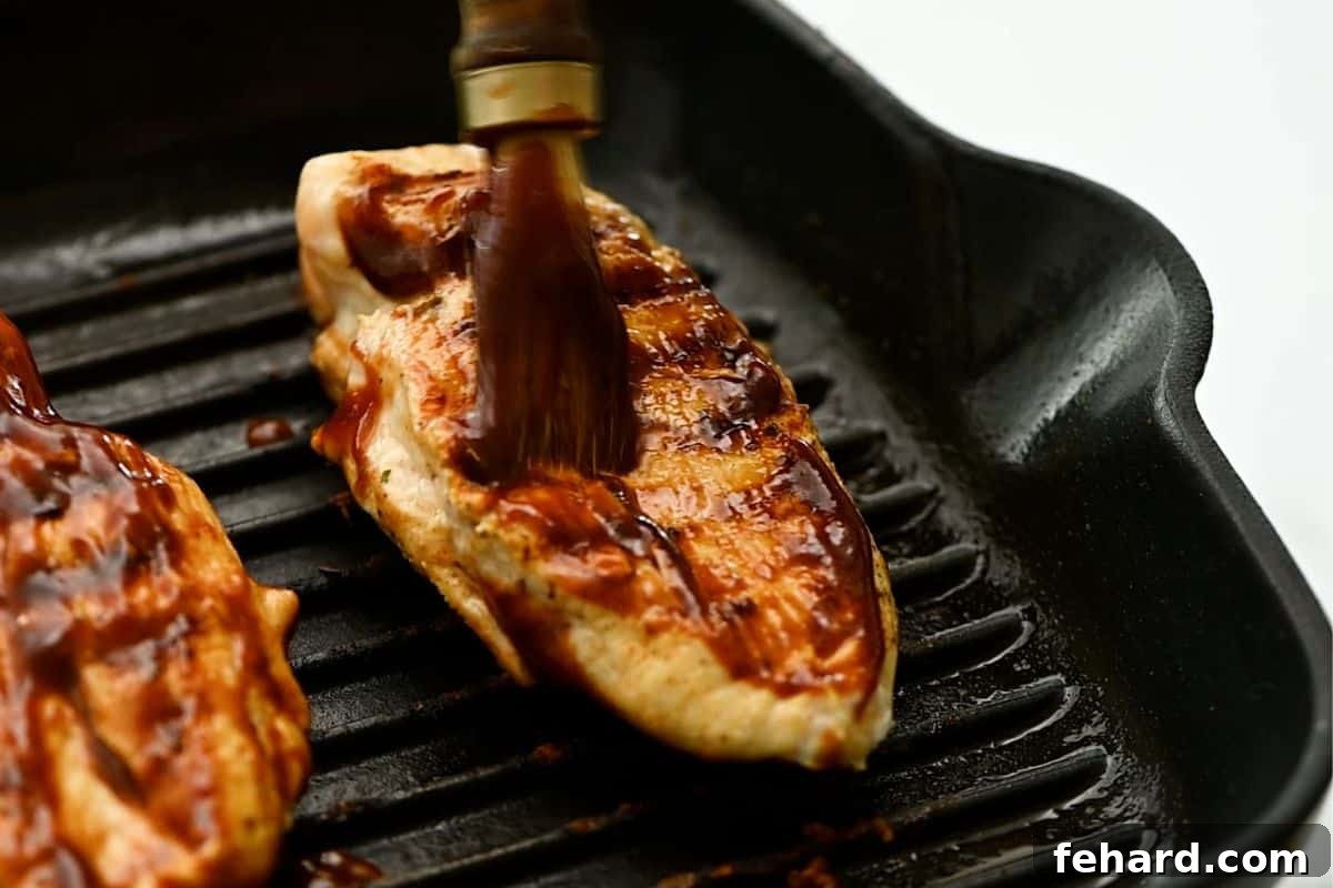 Grilled chicken breasts cooking on a grill pan, being brushed with barbecue sauce for a caramelized finish.