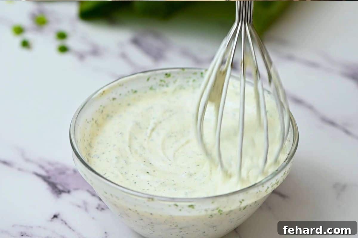 Ranch Dressing Recipe A close-up shot of ranch dressing being combined in a small mixing bowl with a whisk, showcasing its creamy texture.