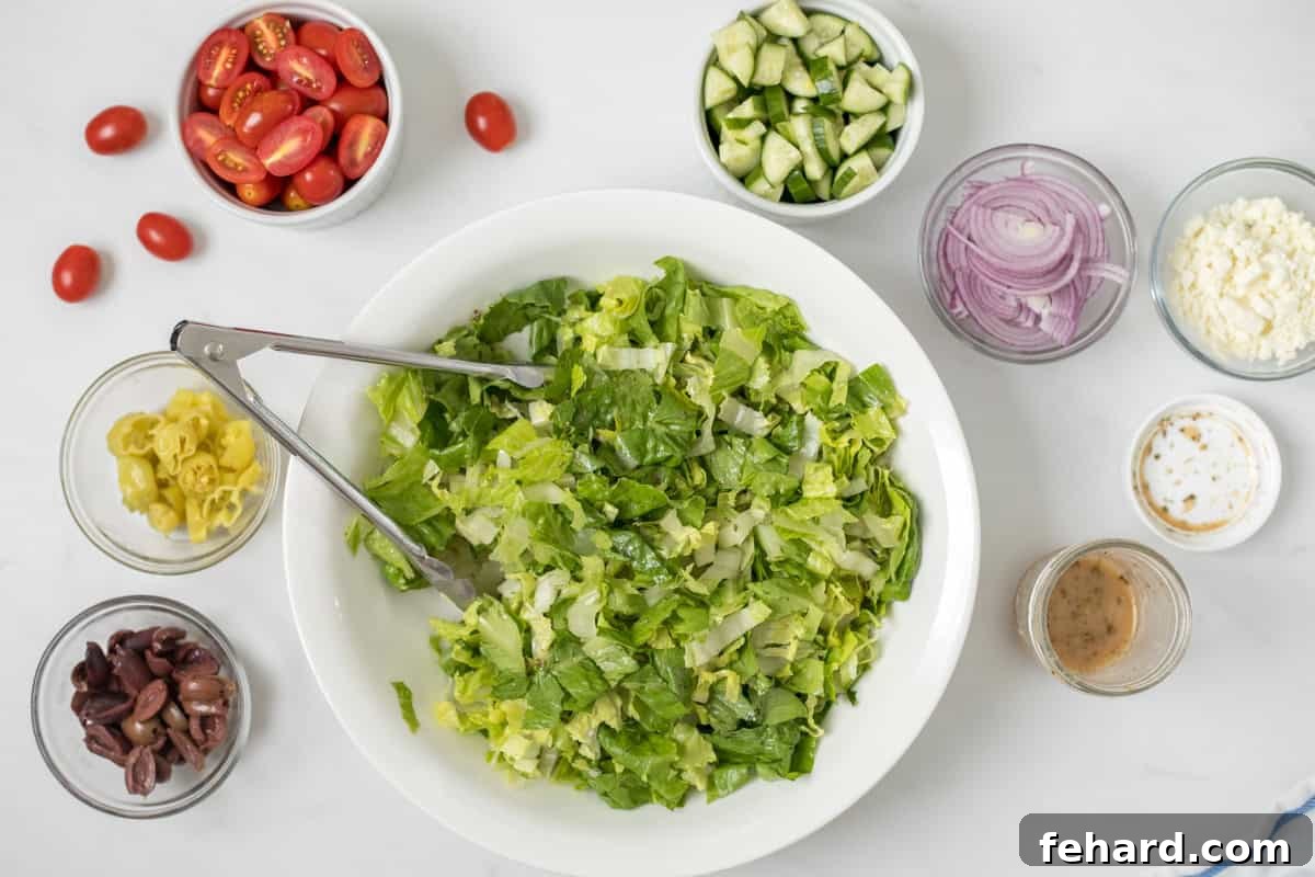 Preparing Panera Greek Salad Base A large mixing bowl containing a generous portion of washed and chopped romaine lettuce, with various components for Panera's Greek Salad neatly arranged around it on a clean surface.