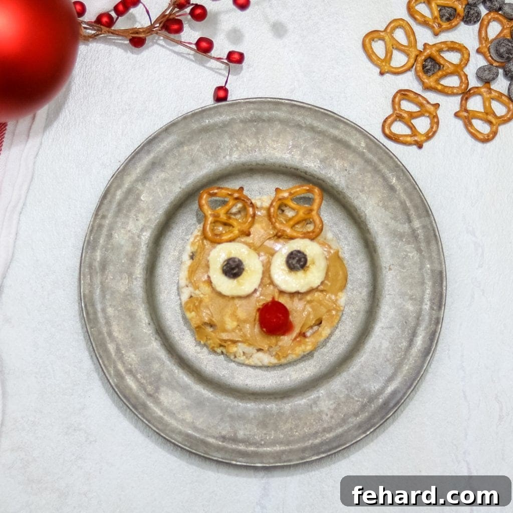 Rice cake spread with peanut butter topped with banana and cherry to look like rudolph. A quick and easy Rudolph-themed snack for kids.