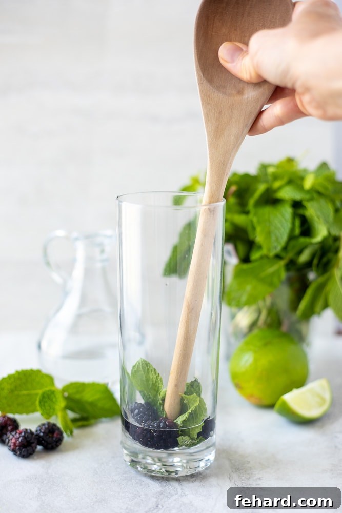 Wooden Spoon Muddling Blackberries and Mint in glass.