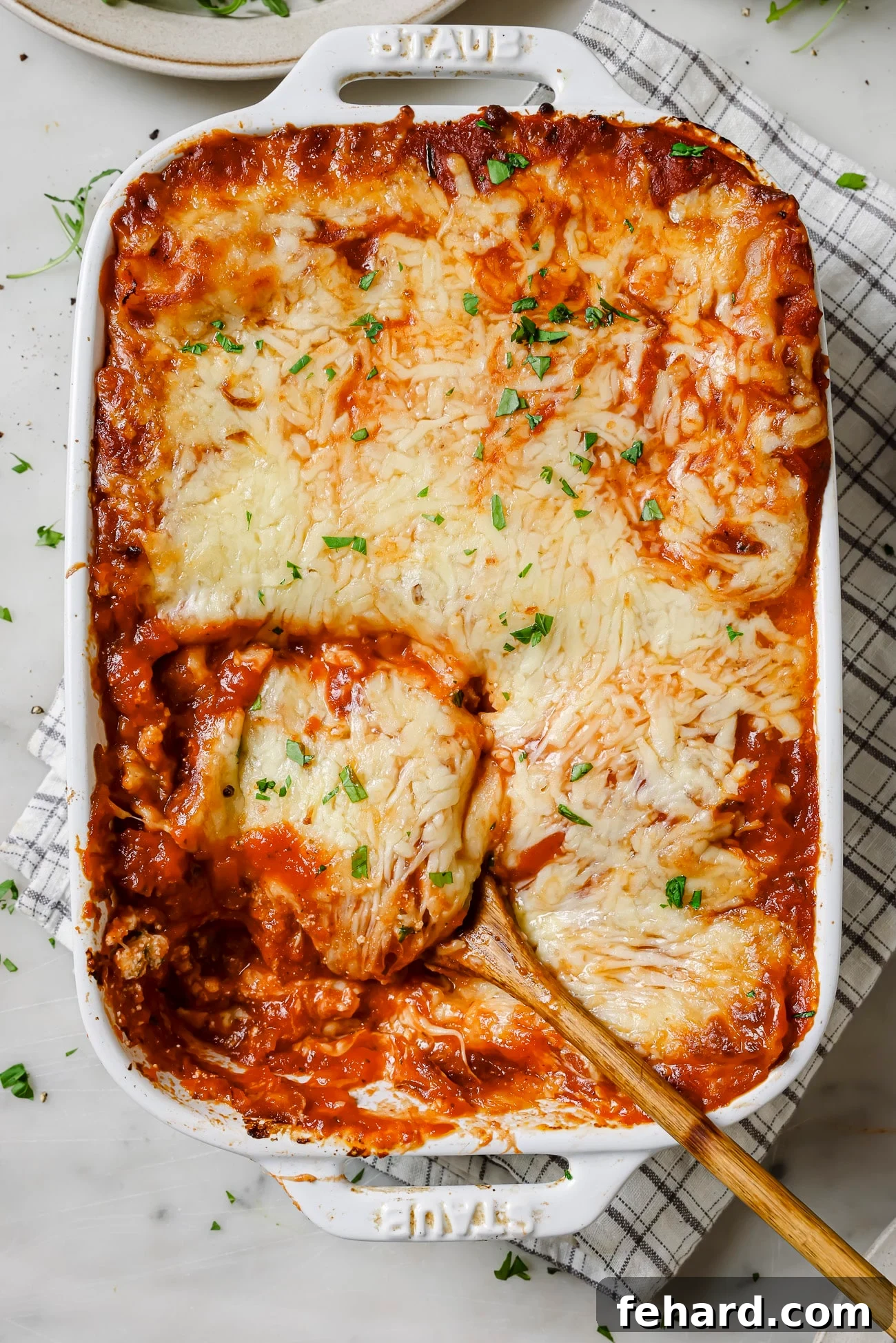A casserole dish of lasagna rolls with a spoon dishing a serving out. 